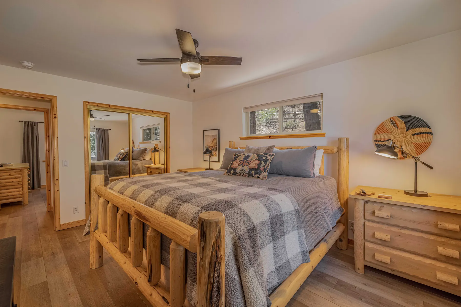 Primary bedroom at Pine Grove Cabin with mountain artwork, reading lamp, and woven wall decor