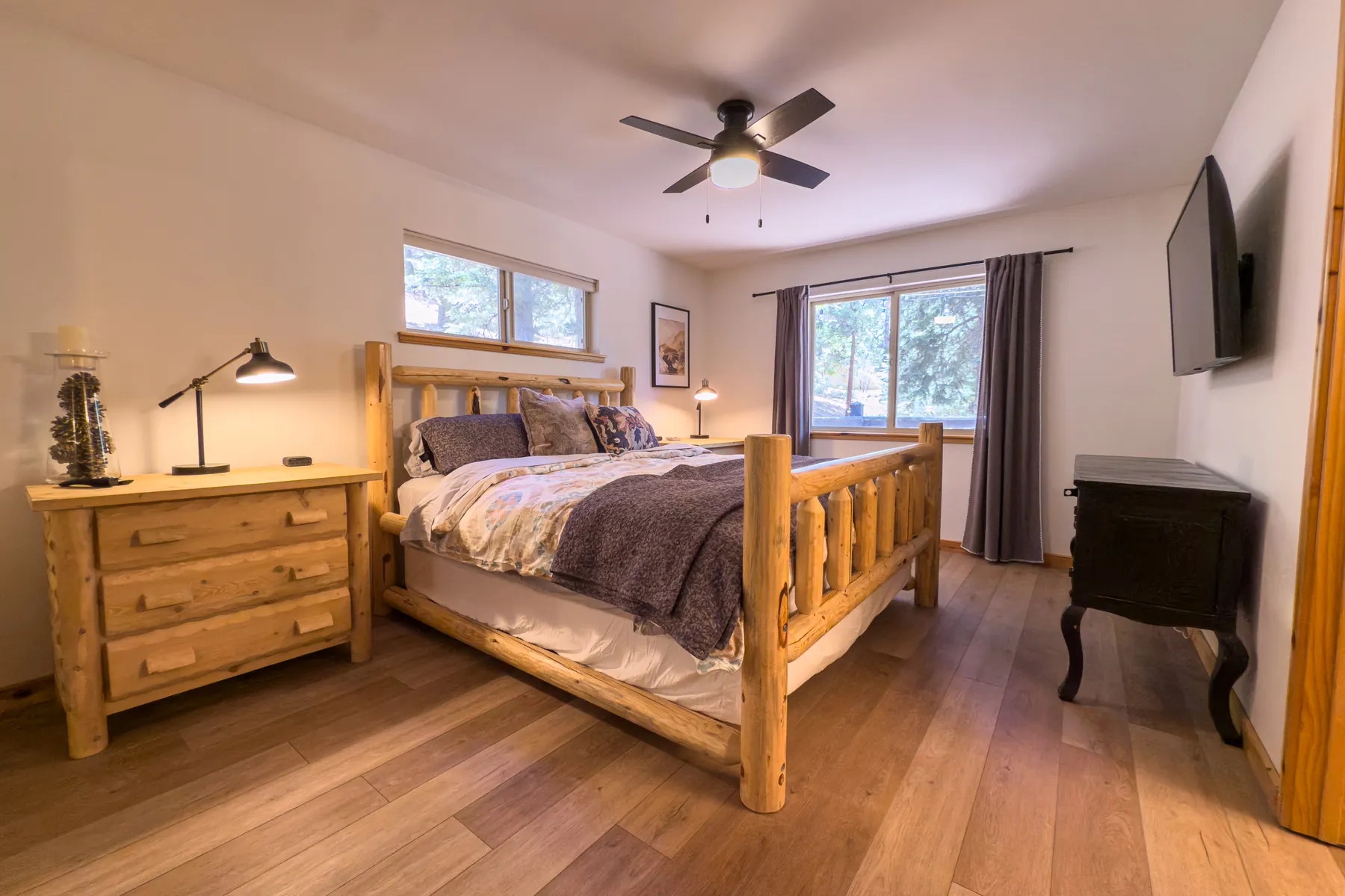 Primary bedroom at Pine Grove Cabin with a king log bed, ceiling fan, dresser, and forest-view windows