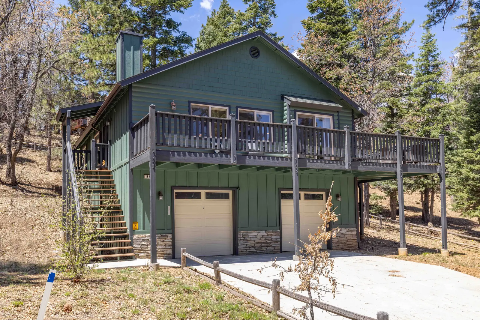 Exterior of Pine Grove Cabin, a green mountain cabin with a wraparound deck, surrounded by tall pines in Moonridge, Big Bear Lake