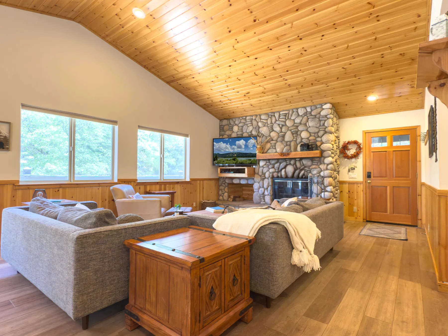 Living room at Pine Grove Cabin with a river-rock fireplace, knotty pine ceilings, and sectional couch