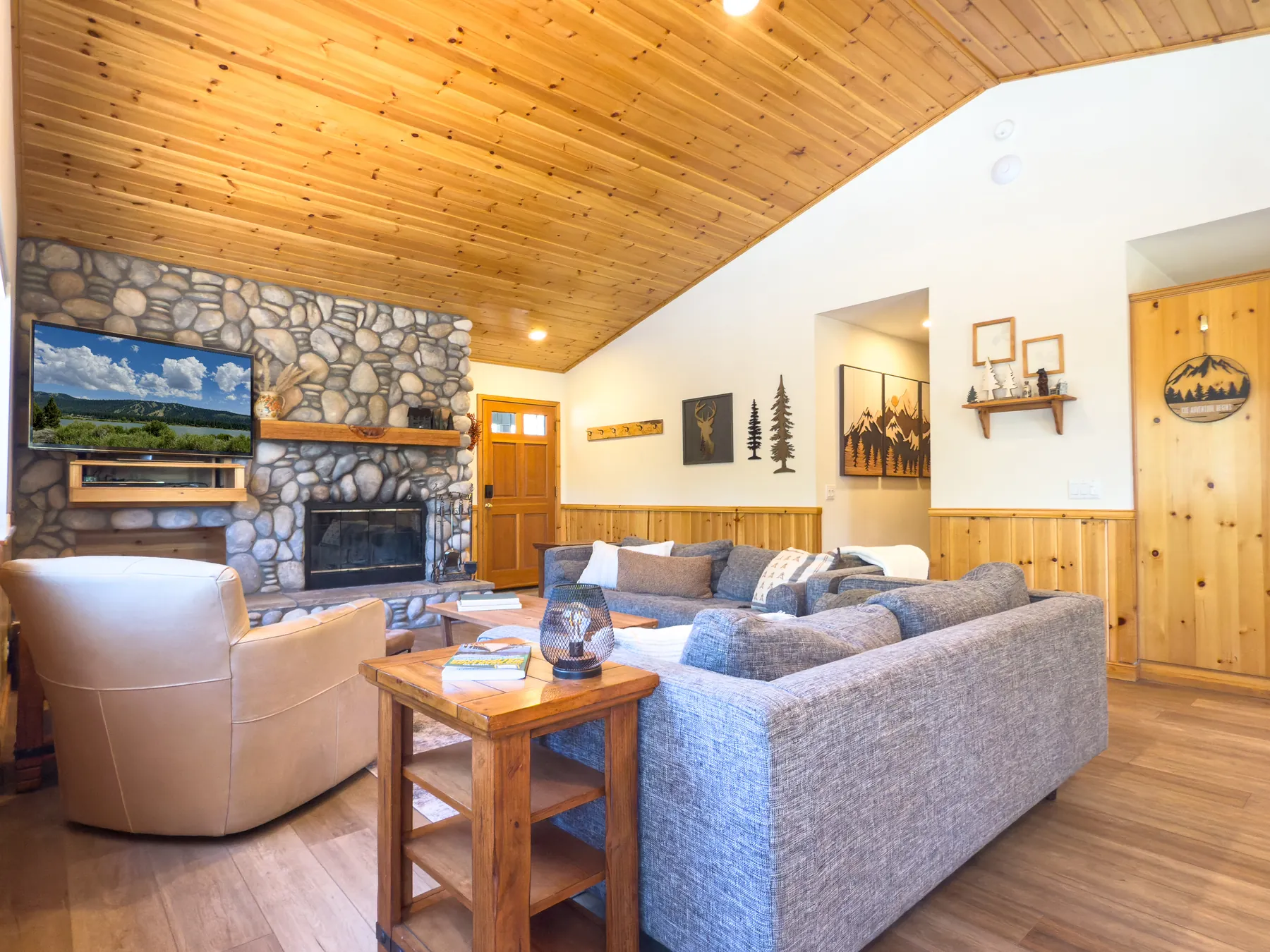 Living room at Pine Grove Cabin showing the stone fireplace, mounted TV, and mountain-themed wall art