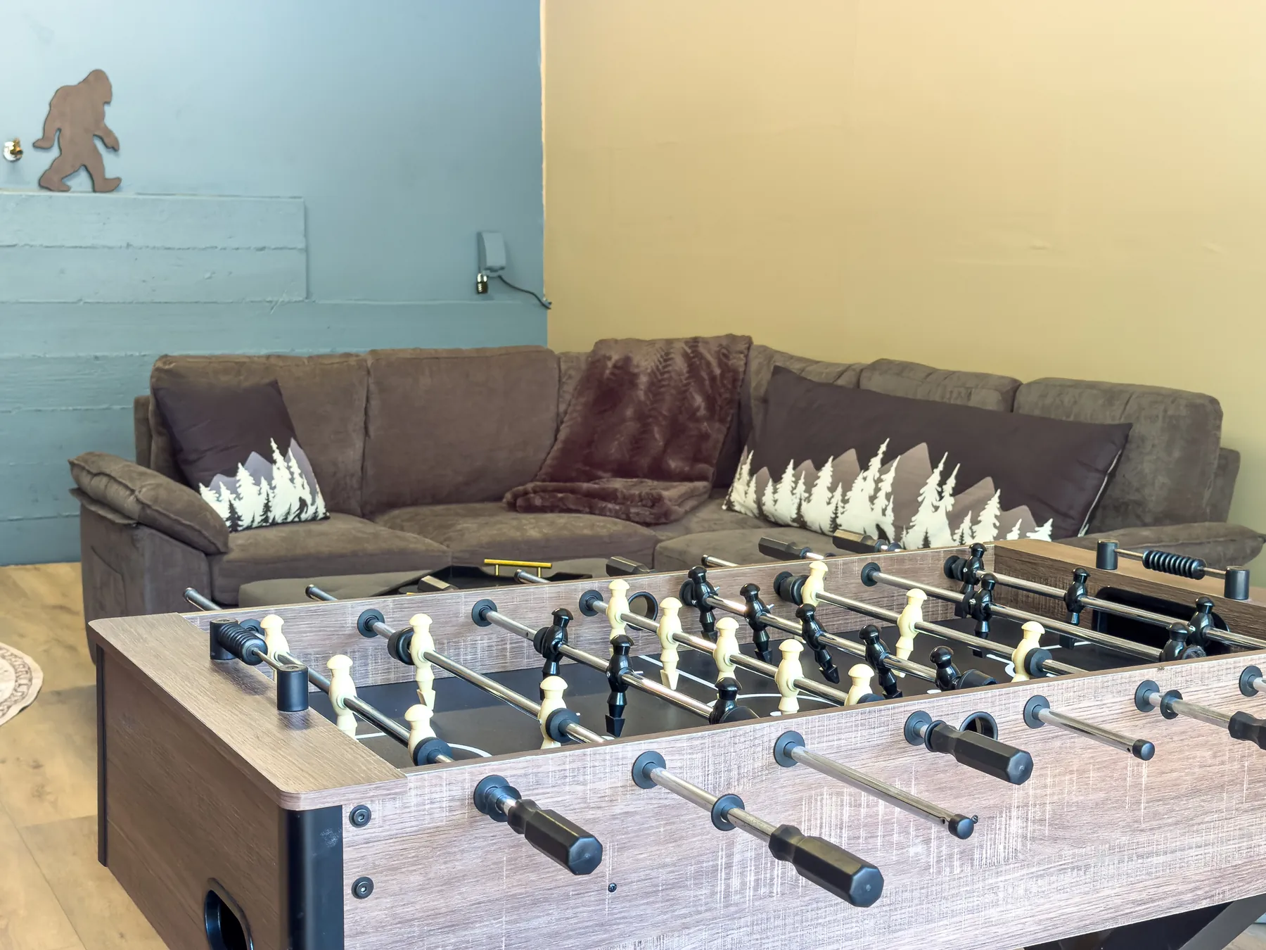 Close-up of the foosball table and sectional couch with mountain and Bigfoot pillows in the Sasquatch Den at Pine Grove Cabin
