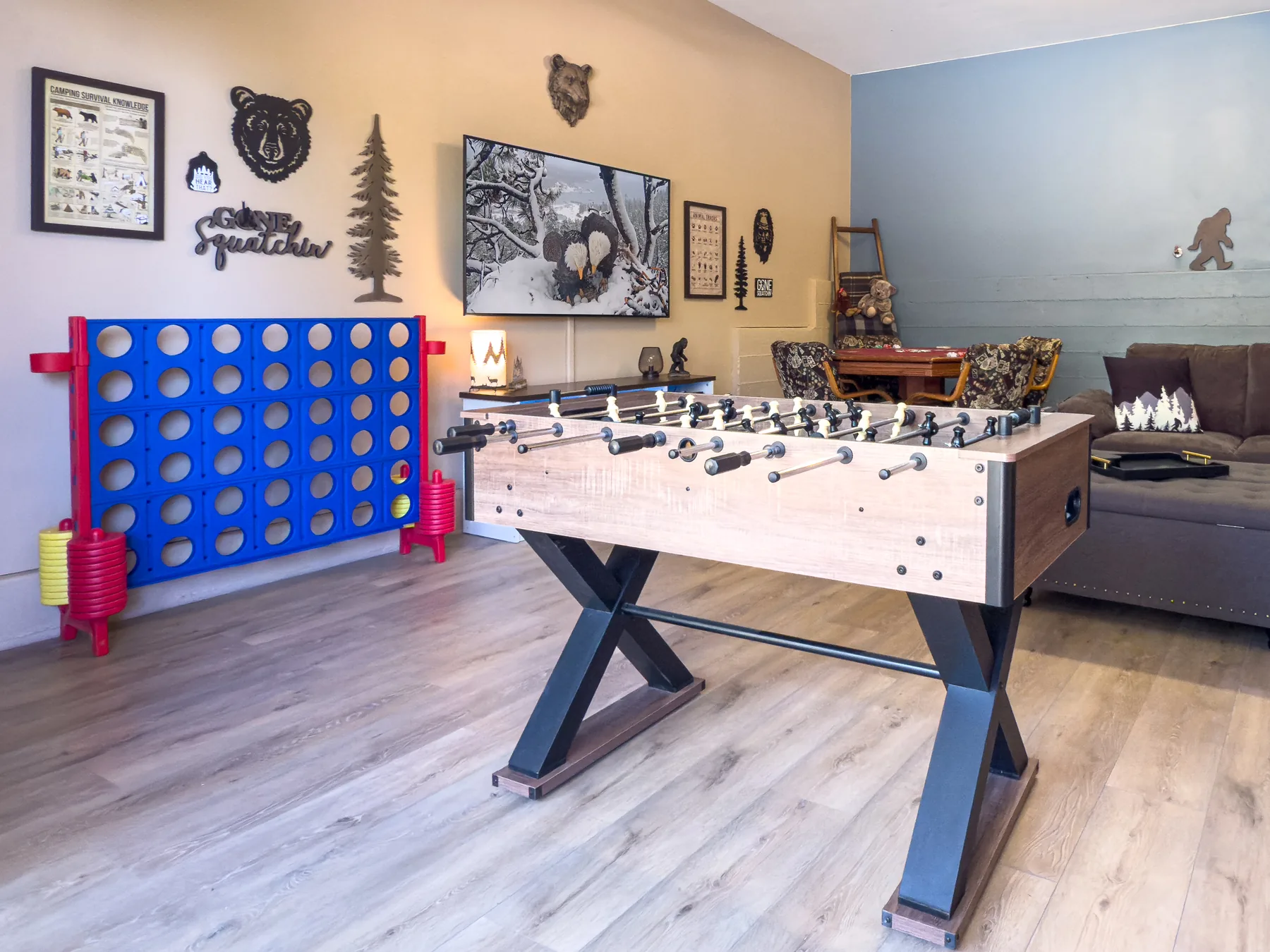 The Sasquatch Den at Pine Grove Cabin, a downstairs game room with a foosball table, jumbo Connect Four, sectional couch, and Bigfoot-themed wall decor
